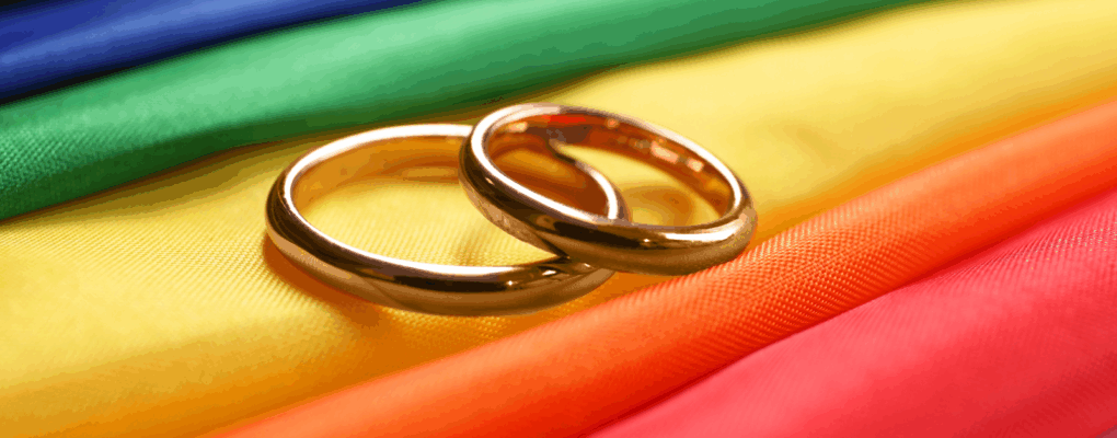 Two gold wedding rings on rainbow LGBTQ+ flag.