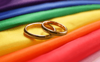 Two gold wedding rings on rainbow LGBTQ+ flag.