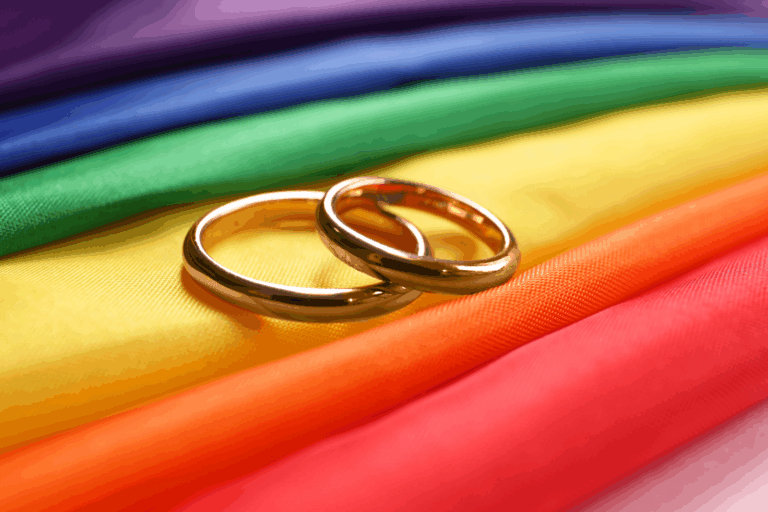 Two gold wedding rings on rainbow LGBTQ+ flag.